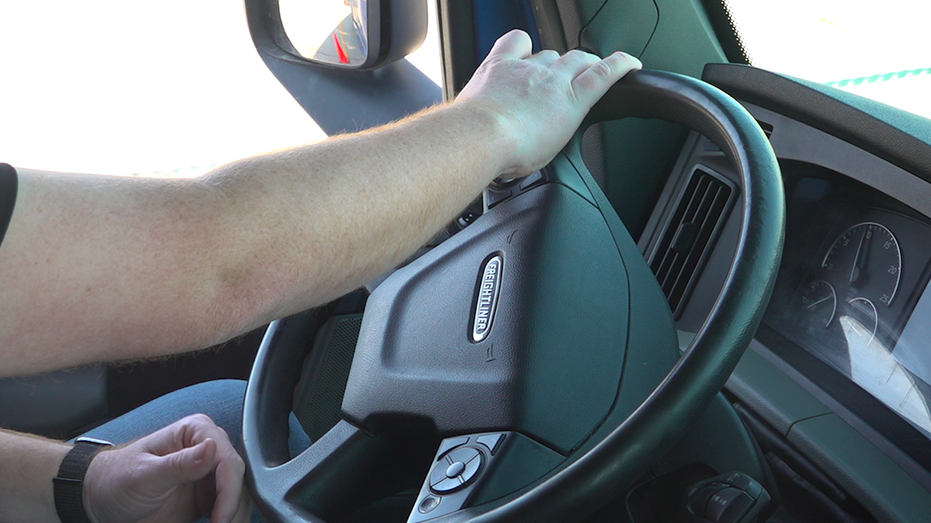 A truck driver with this hand on the wheel