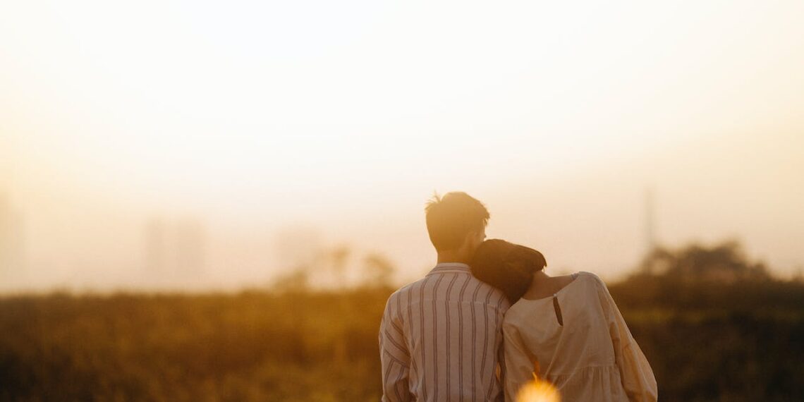 Pareja abrazandose sentados frente a puesta de sol