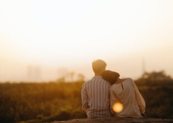 Pareja abrazandose sentados frente a puesta de sol